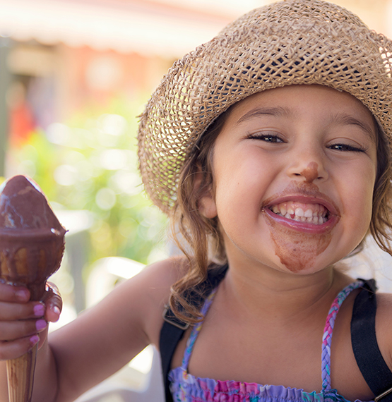 girl smiling holding chocolate ice cream cone and ice cream smeared on her face