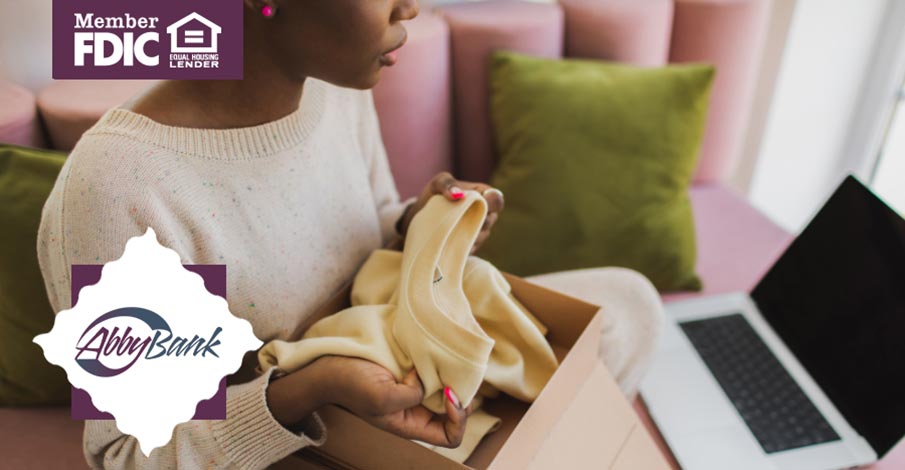 young African American woman looking at sweater she bought online and laptop open near her