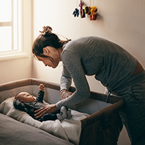 young mother checking on small baby in bassinet