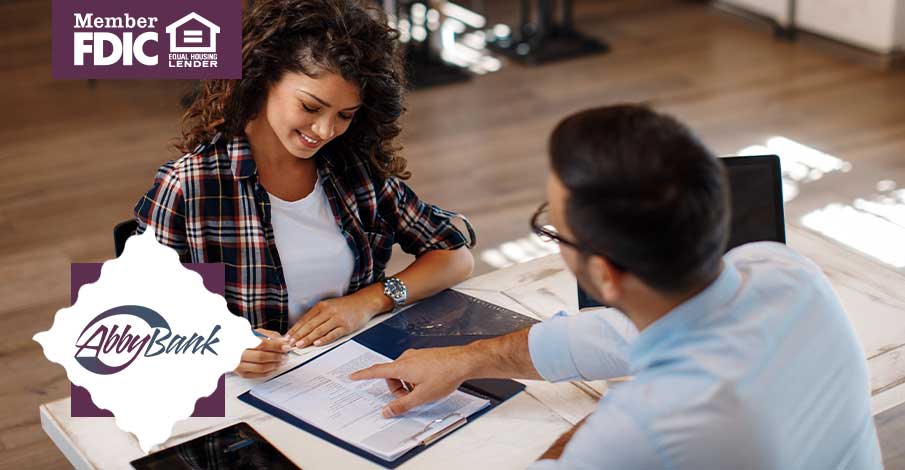 young woman signing papers with a male banker pointing out where to sign