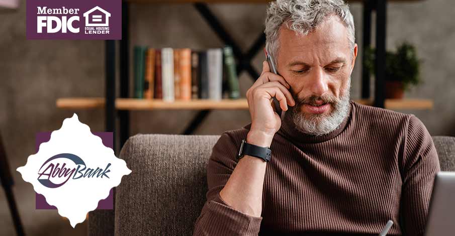 middle aged man talking on phone while sitting on couch looking at laptop