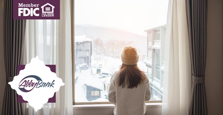 young girl or woman in hat and sweater looking out apartment window at winter weather scenery outside