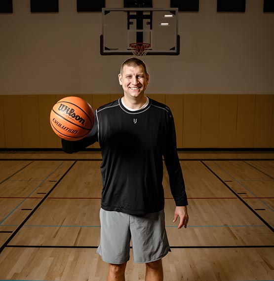 Brian Butch standing on basketball court holding a basketball out in his hand while smiling
