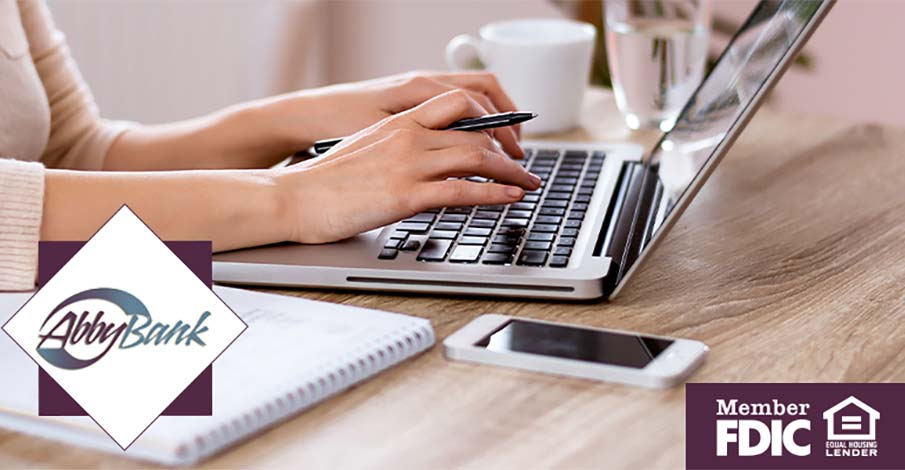 woman typing on laptop at desk with pen in hand and mobile phone and notebook nearby