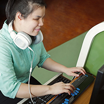 young blind Asian woman with headphones smiling using braille keyboard device