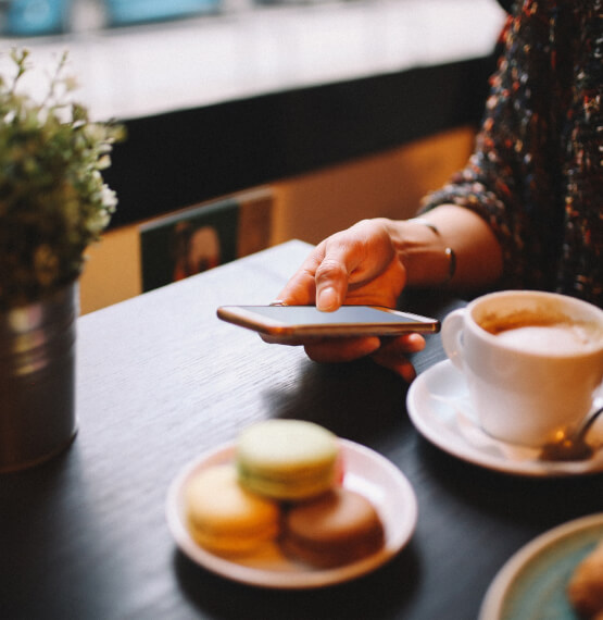 Woman using phone next to coffee and cookies
