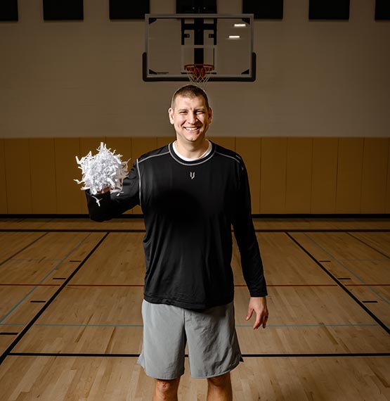Brian Butch on a basketball court holding up a fistful of shredded paper