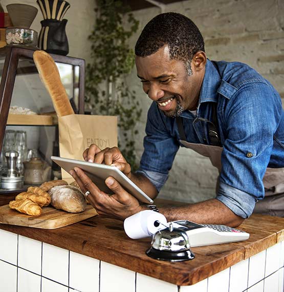 happy black business owner looking at tablet in bakery